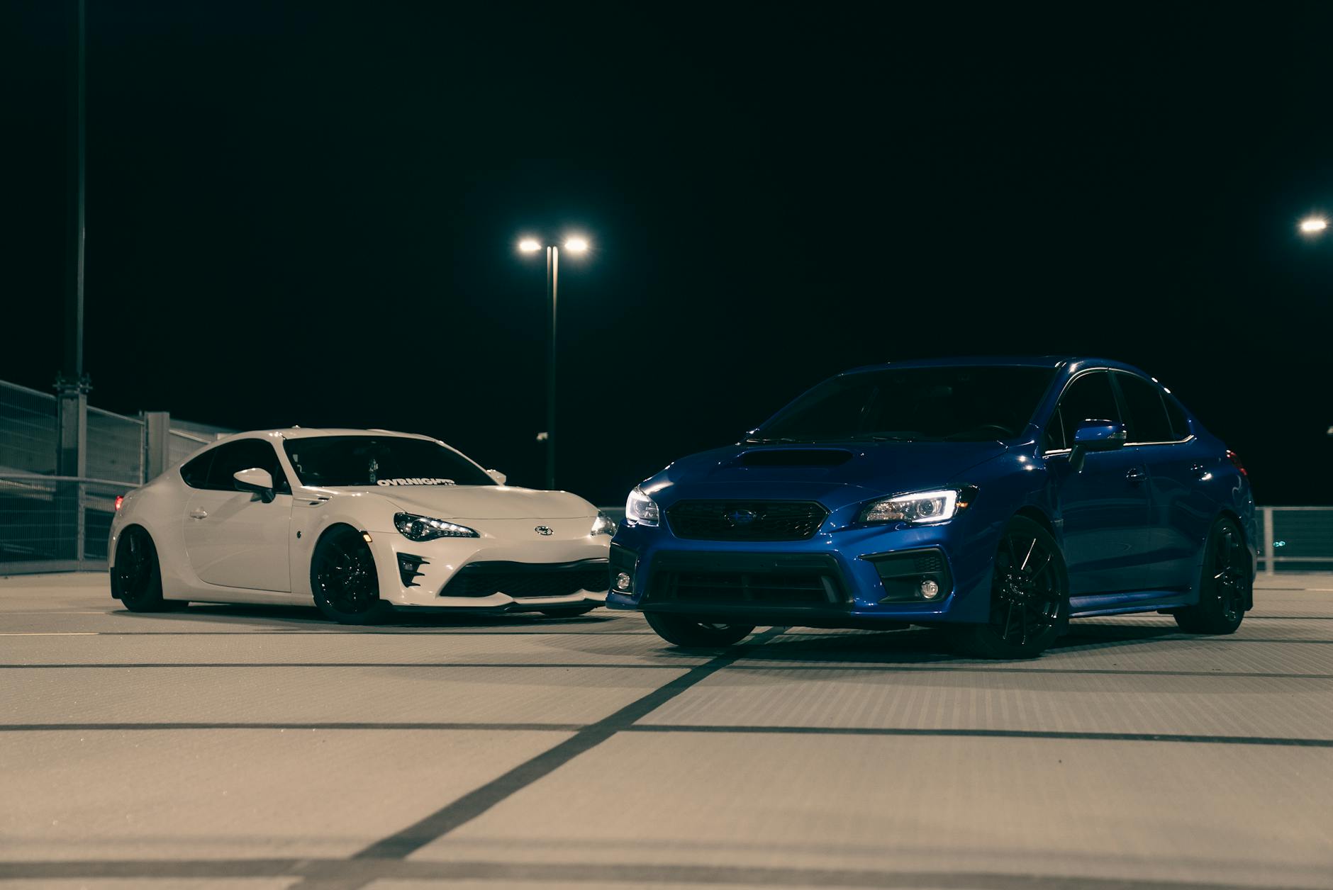 Dwa sportowe Nissany na dachu parkingu nocą pod latarniami