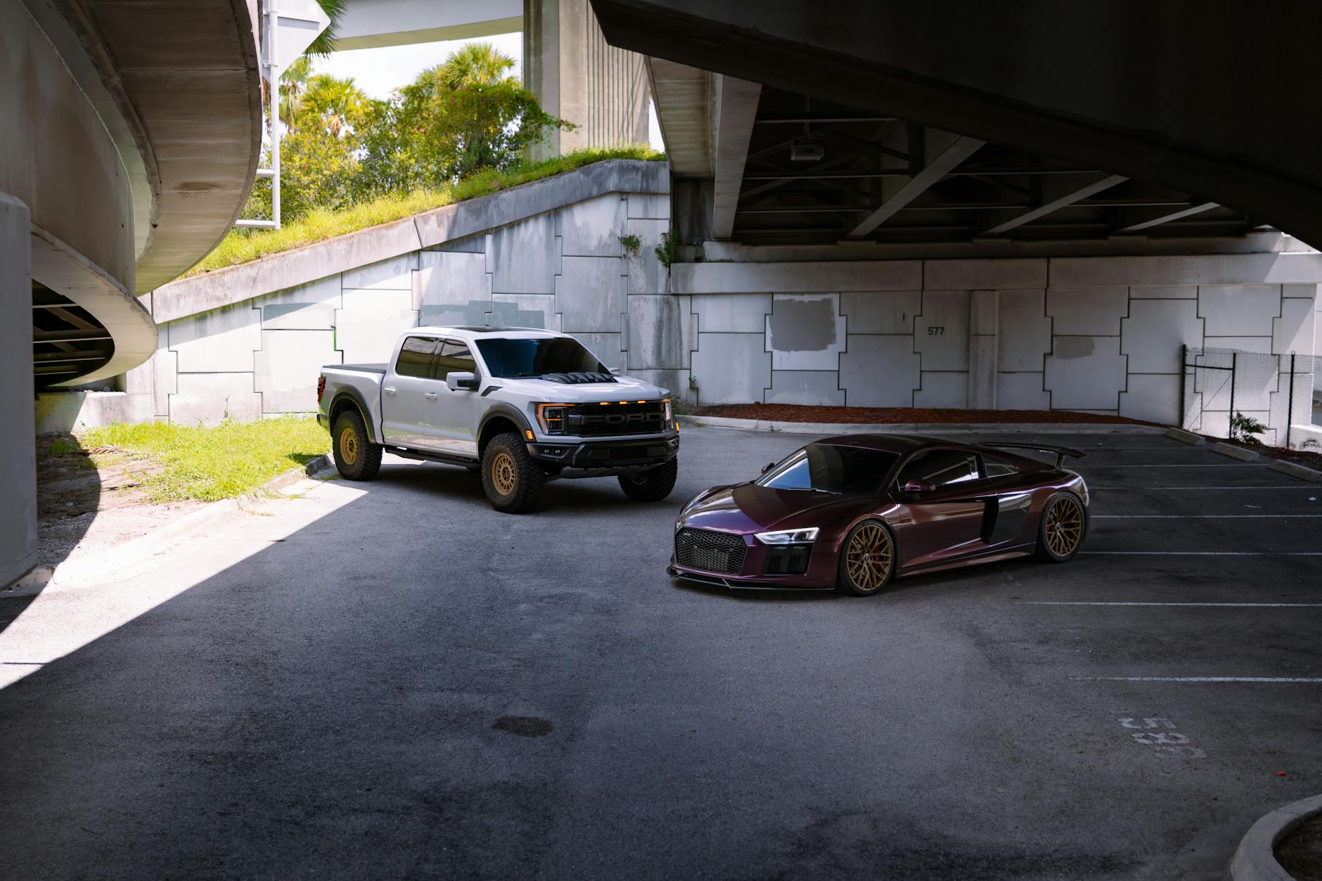 Srebrny pickup i czerwone sportowe auto zaparkowane pod miejską estakadą