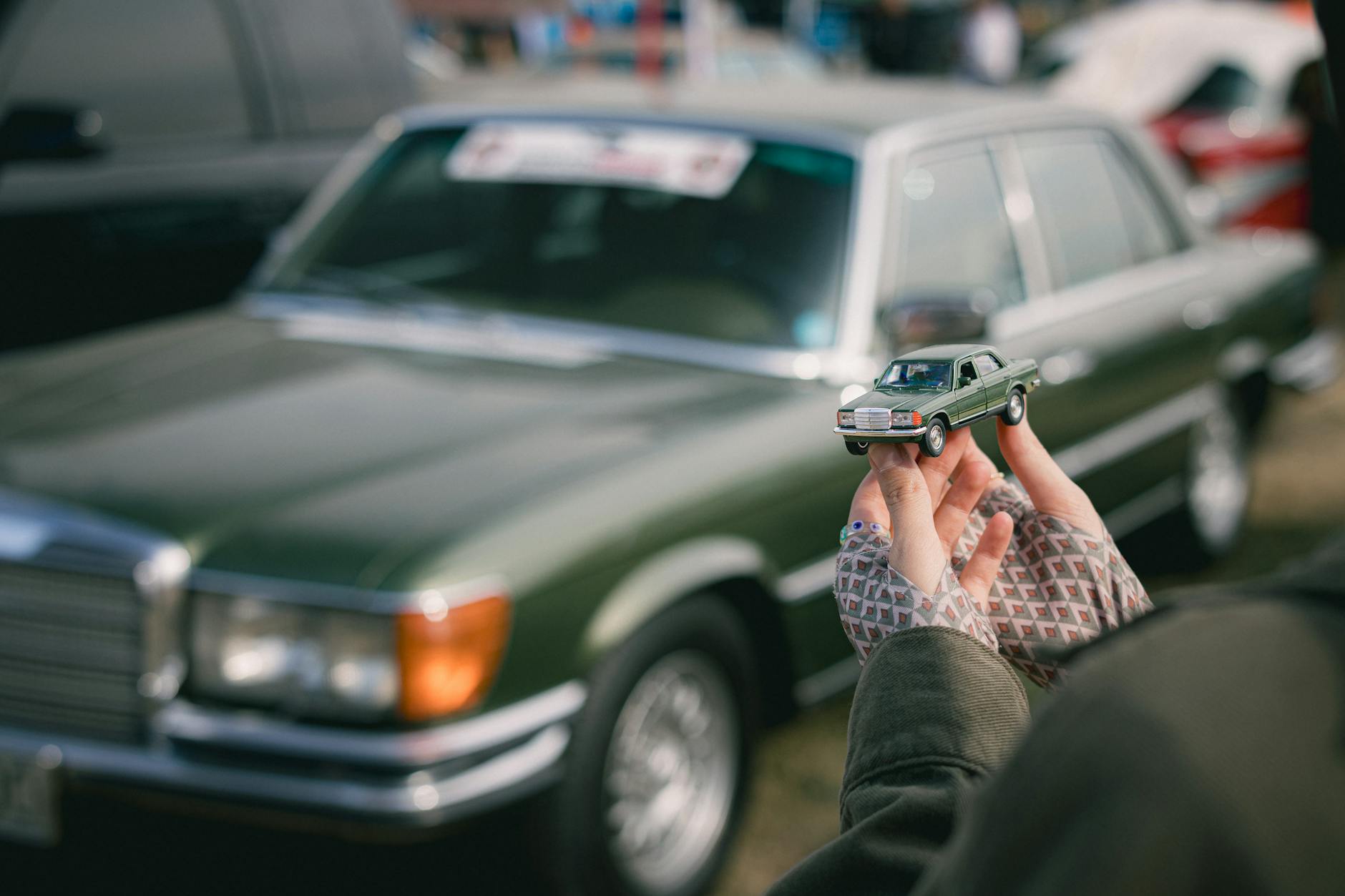 Zielony klasyczny Mercedes i dopasowany modelik trzymany w dłoniach