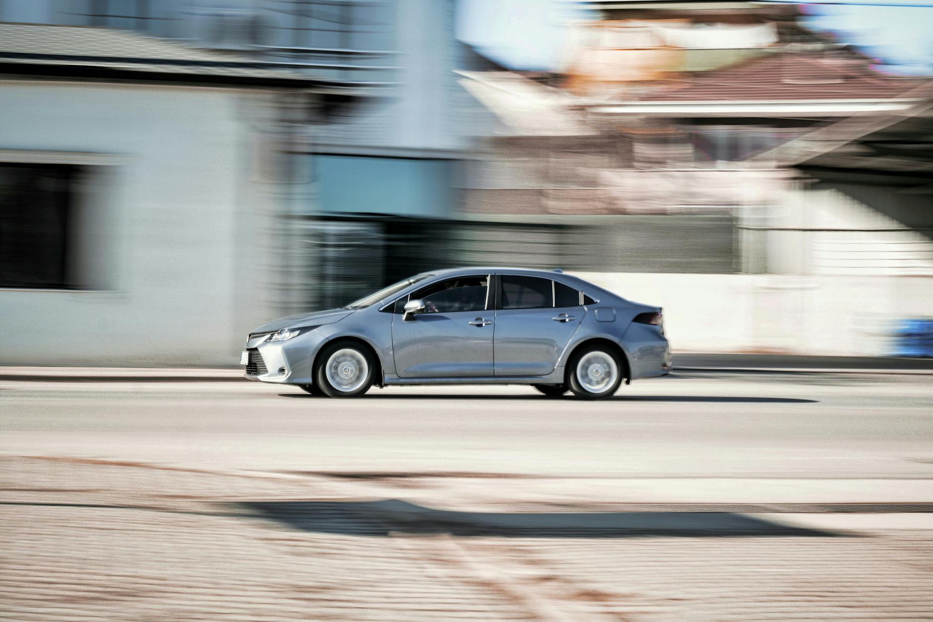 Srebrna Mazda 6 jedzie szybko po miejskiej ulicy z efektem rozmycia ruchu
