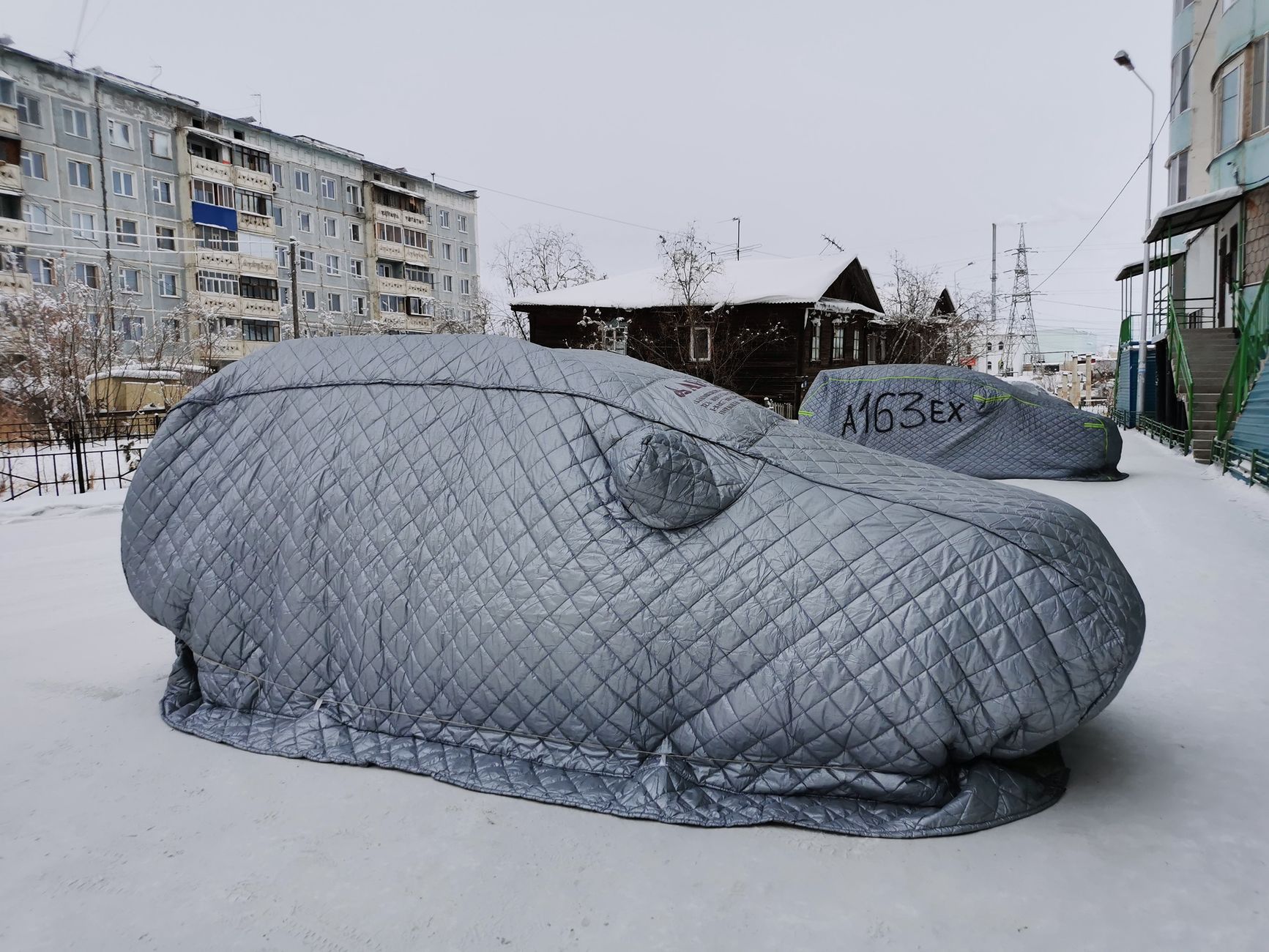 BYD a polska zima realny spadek zasięgu ogrzewanie pompy ciepła i praktyczne triki kierowców Samochody BYD pod śniegiem z zimowymi pokrowcami w miejskiej scenerii