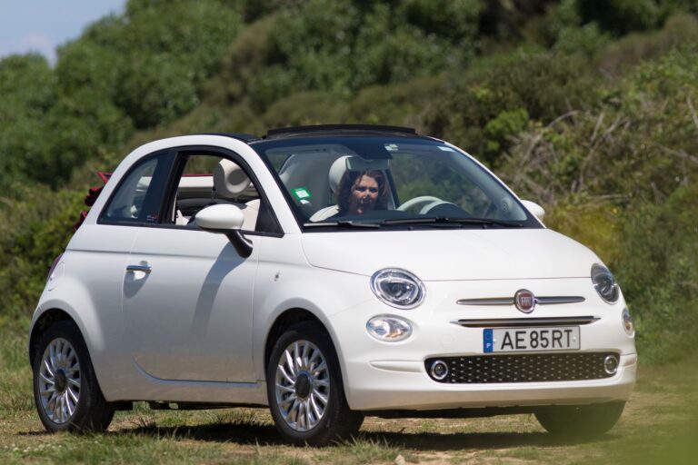 Biały Fiat 500 z otwartym dachem na słonecznej drodze wśród zieleni